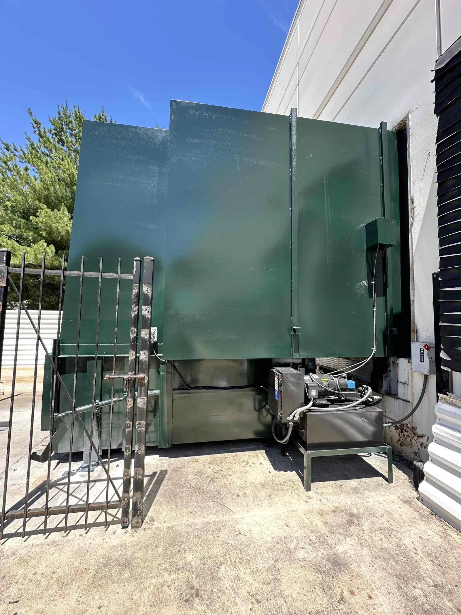 A green compactor installed beside a building