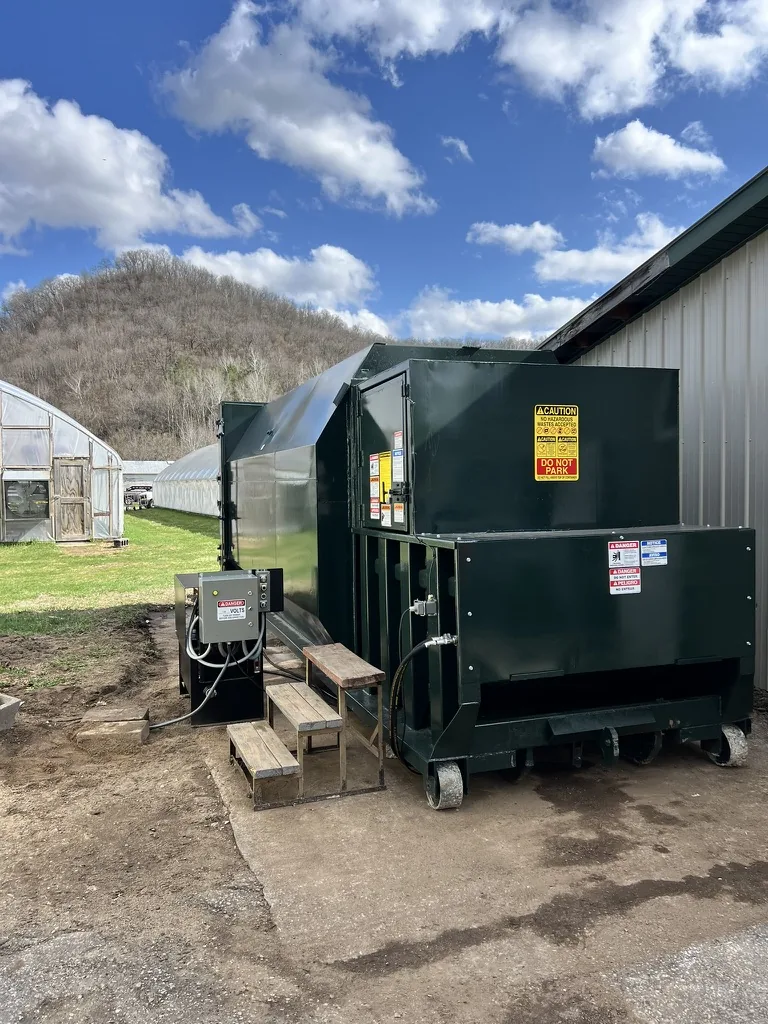 A green compactor installed outside a building
