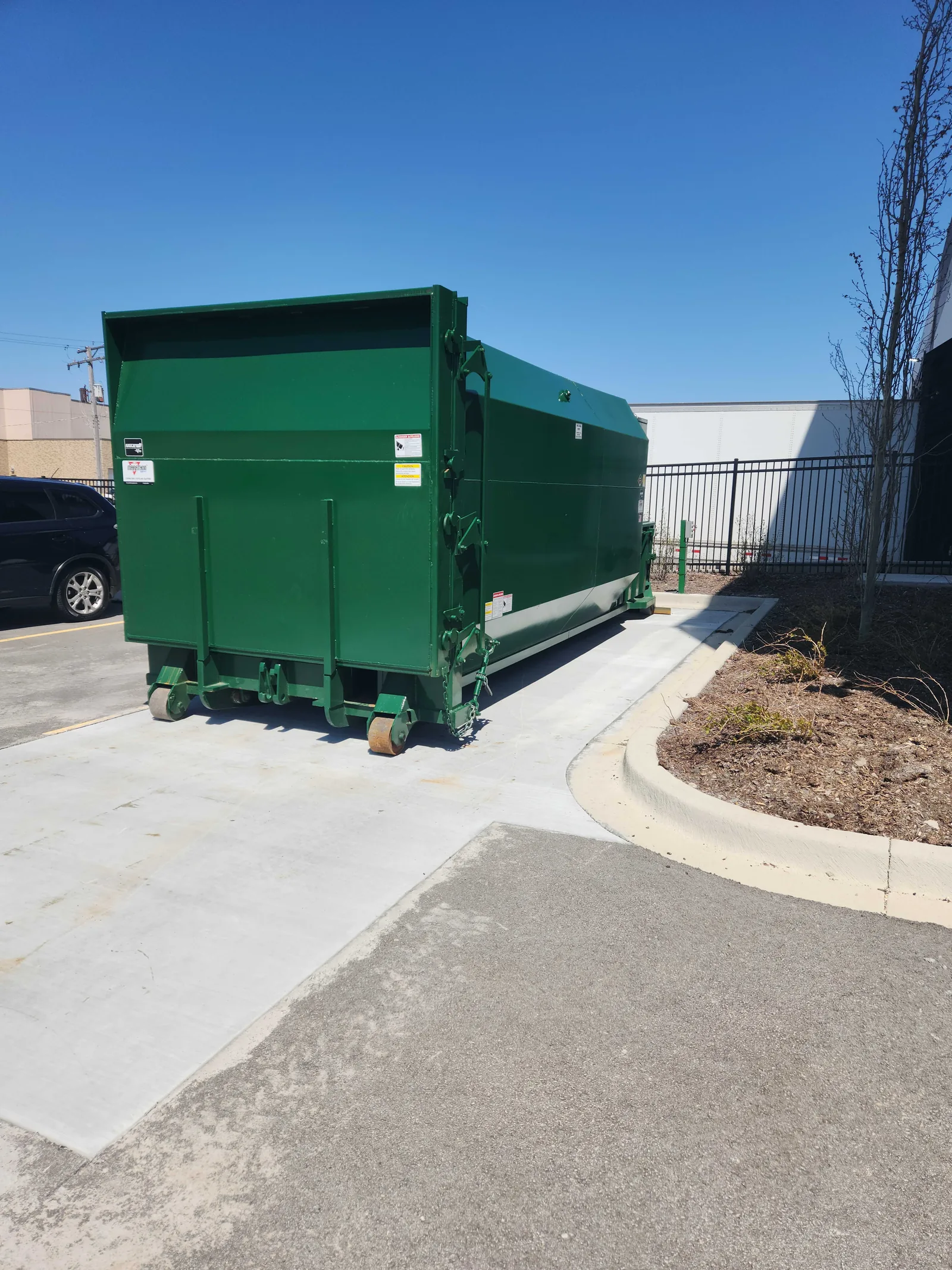 A green compactor container in a parking lot