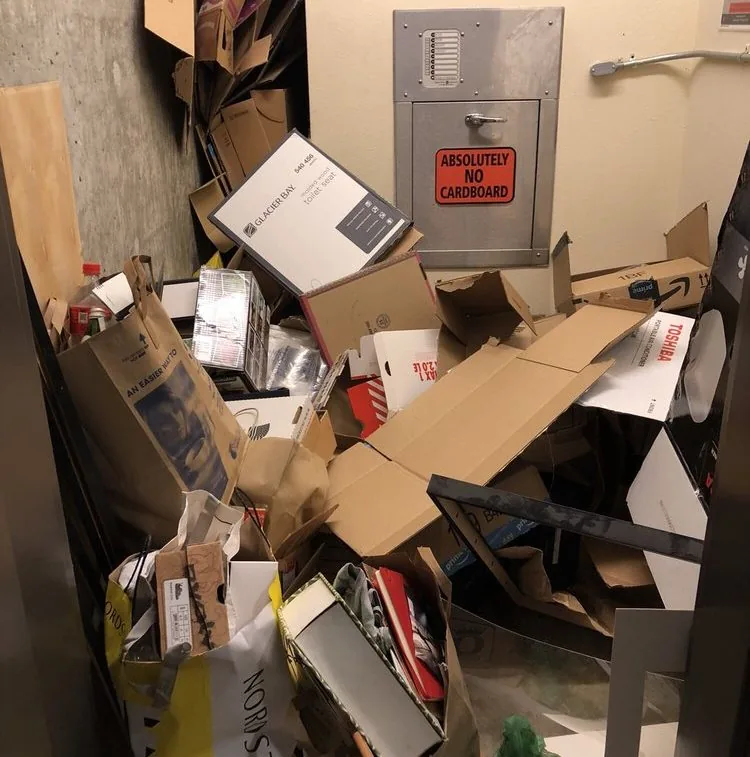 Cardboard piled up in a high rise trash room beside the chute